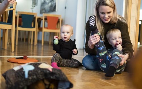 Några mammor sitter på golvet med sina bebisar.