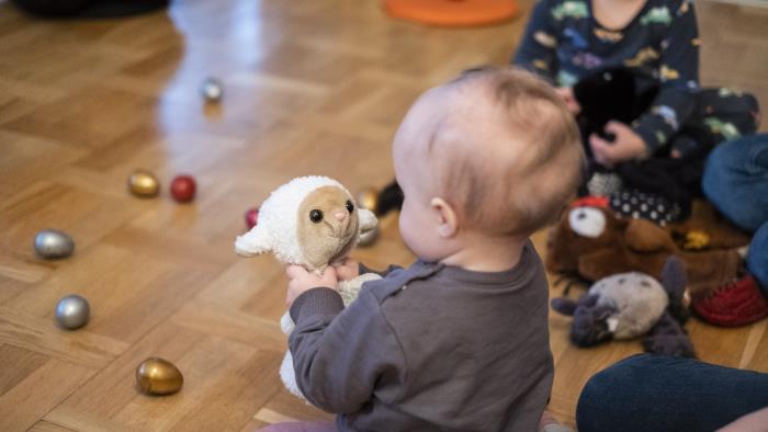 En bebis på golvet tittar på ett gosedjur som föreställer ett får.