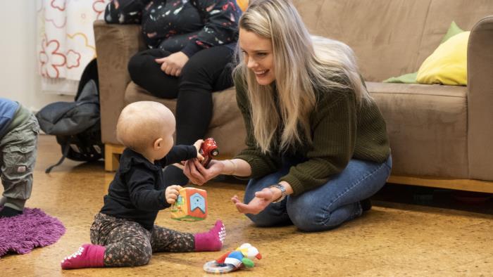 En mamma sitter på golvet och leker med sin bebis.