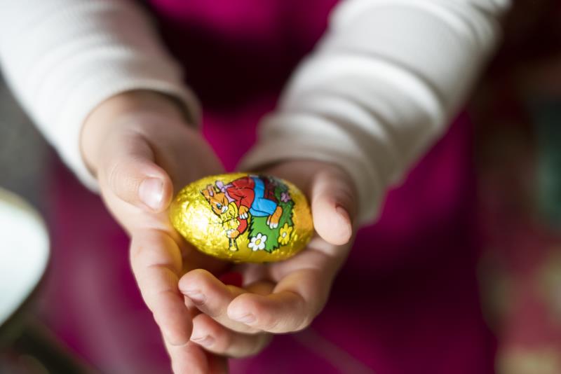 Ett barn håller i ett chokladägg inslaget i guldfolie med påskmotiv.