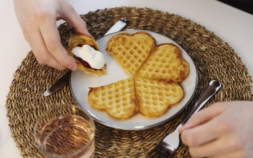 Någon äter våfflor med sylt och grädde.