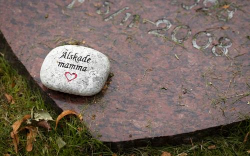 Liten sten med texten "älskade mamma" inristad ligger på en gravsten.