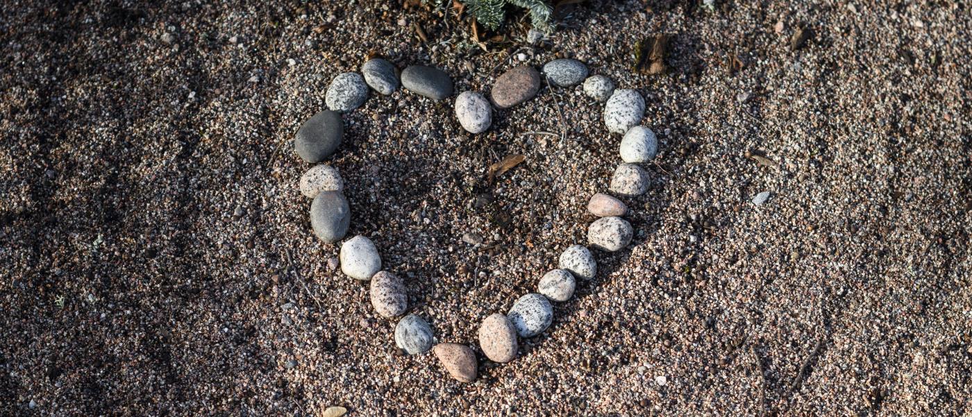 Stenar upplagda i form av ett hjärta framför en krans på en grav.