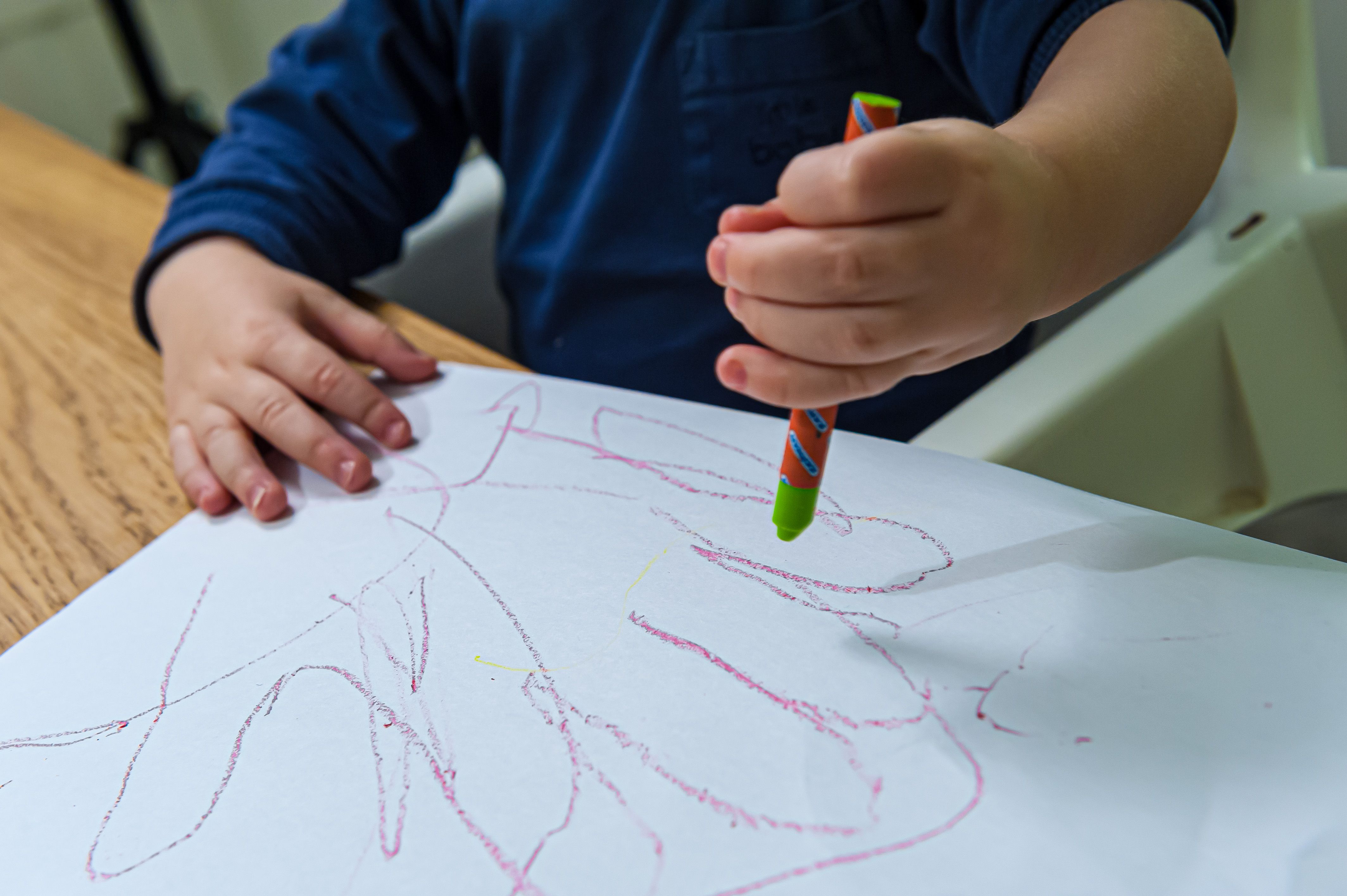 Ett barn ritar med kritor på ett papper.