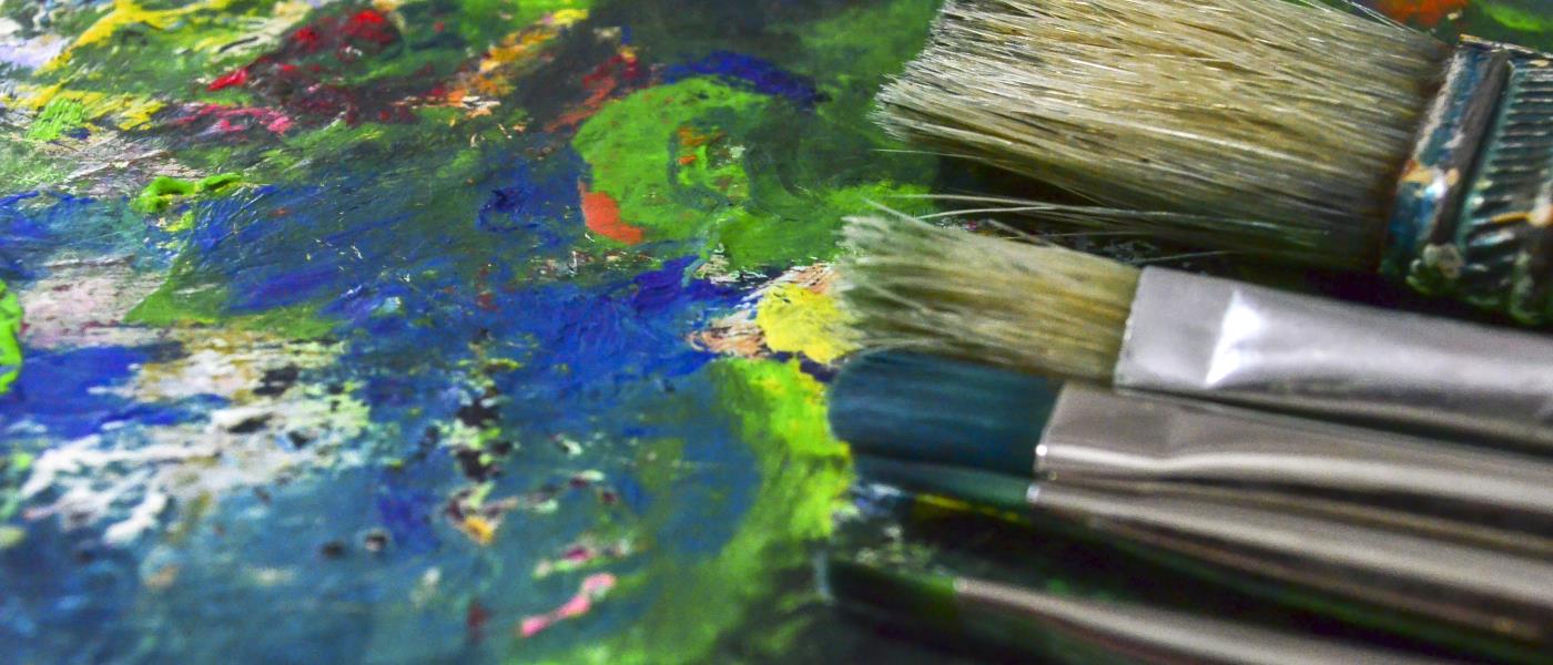 Närbild av målarpenslar på en palett fylld av torkad färg.
