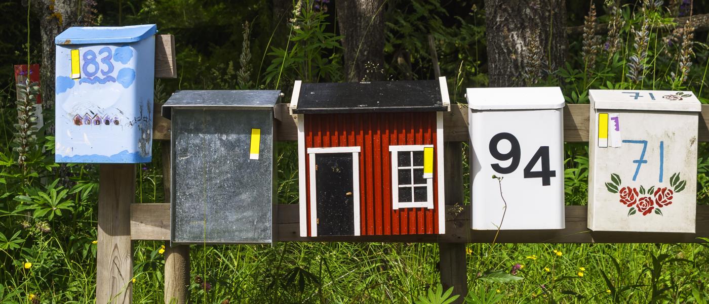 Fem färgglada brevlådor bredvid varandra. Kanske till sommarstugor.