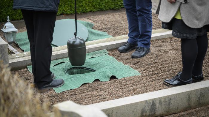 Någon sänker ner en urna i marken på en gravplats.