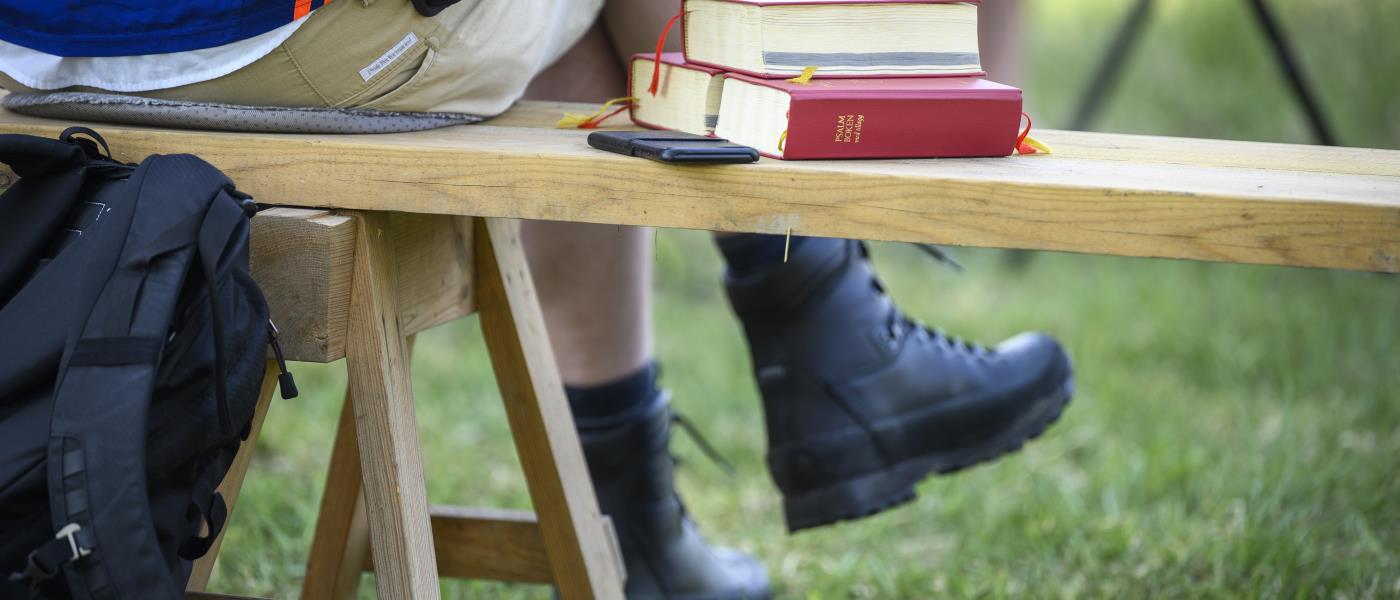 Någon sitter på en bänk utomhus. Bredvid ligger några psalmböcker.