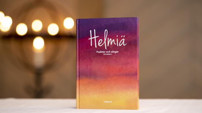 En färgglad bok med psalmer och sånger på finska står uppställd på ett bord i en kyrka.