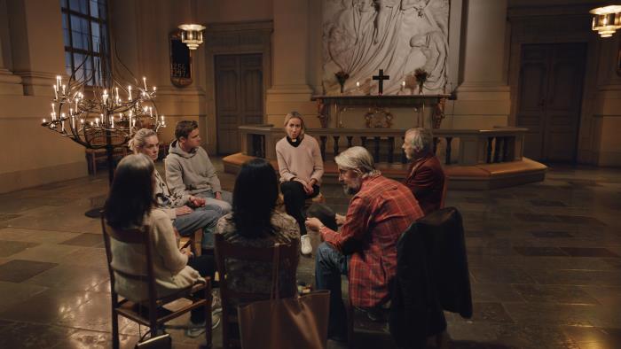 Några personer och en kvinnlig präst sitter på stolar i en ring i en kyrka.