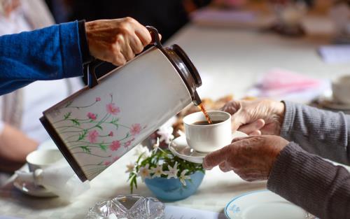 Någon häller upp kaffe från en blommig termos till någon som håller fram sin kopp.