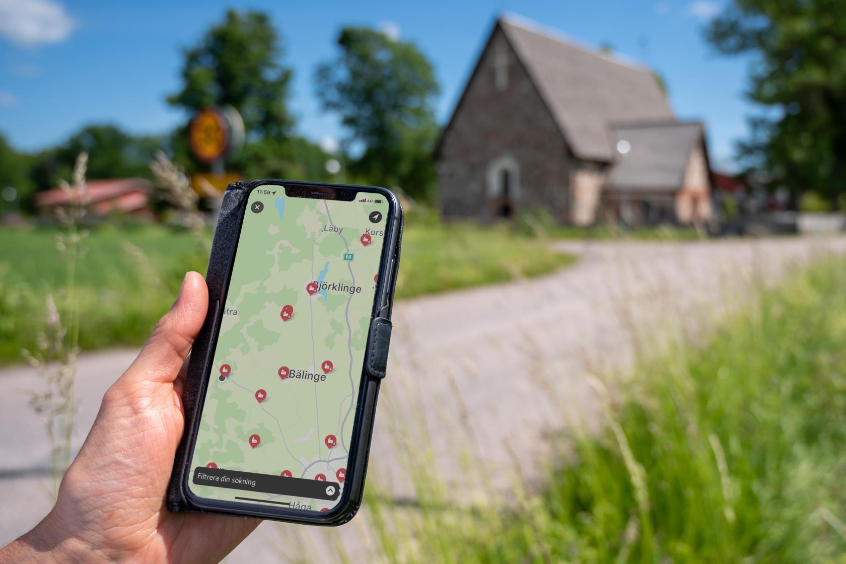 En person som kommit fram till en gammal kyrka håller en mobiltelefon i handen. På skärmen visas kyrkans position på en karta.