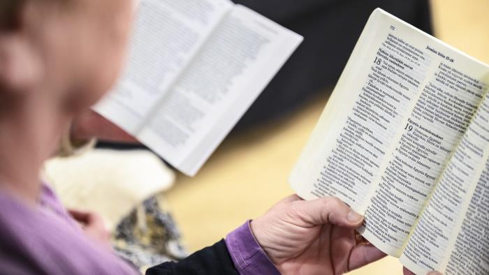 Närbild på någon som läser en bibel i kyrkbänken.