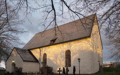 Tre personer går utanför en vit kyrka.