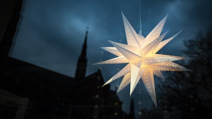 En adventsstjärna lyser i ett fönster. Ett kyrktorn syns i bakgrunden.