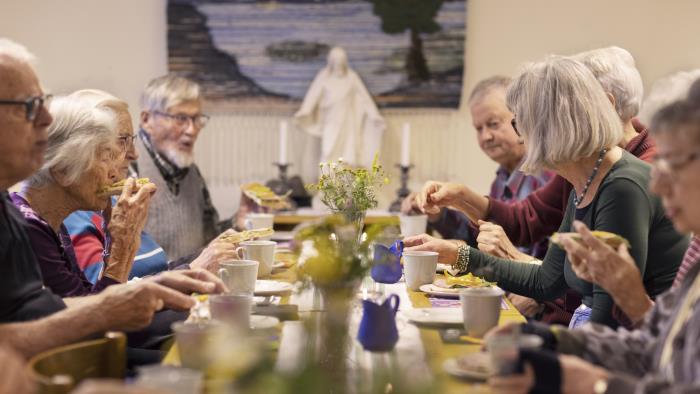 En grupp äldre personer sitter vid ett bord och fikar tillsammans.