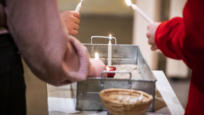 Några personer placerar tända stearinljus i en liten plåtlåda fylld med sand.