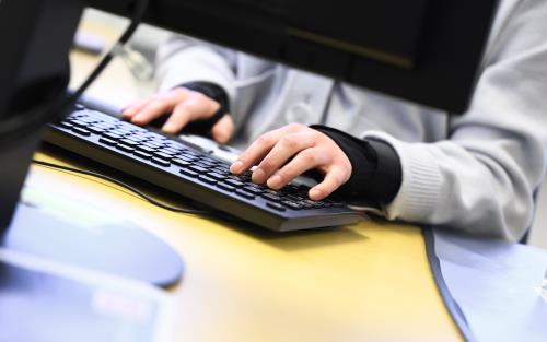 Någon sitter vid ett skrivbord bakom en datorskärm och knappar på ett tangentbord.