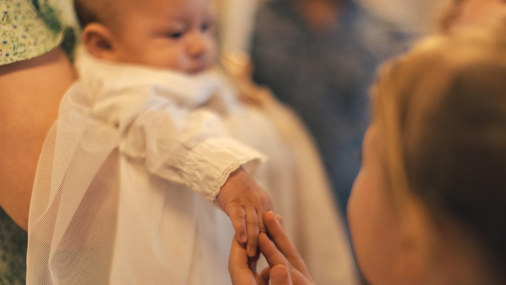 En bebis i dopklänning. Någon håller i barnets hand.