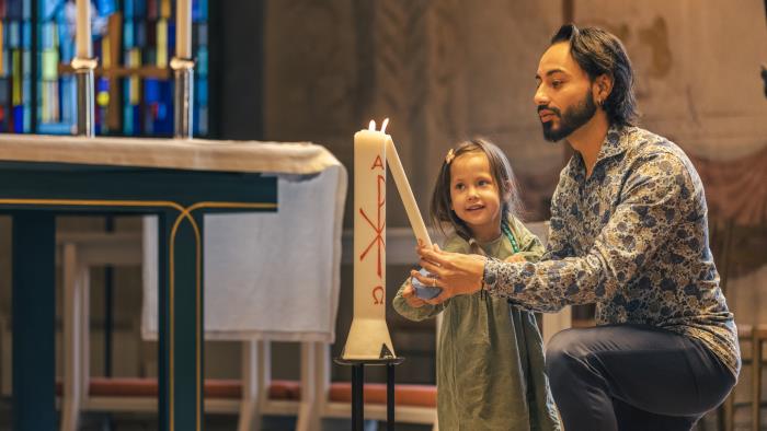 En man och en liten flicka tänder ett dopljus i kyrkan.