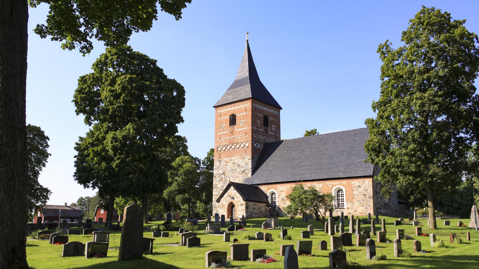 En kyrka i sten och rött tegel. Gravstenar på en grön gräsmatta.