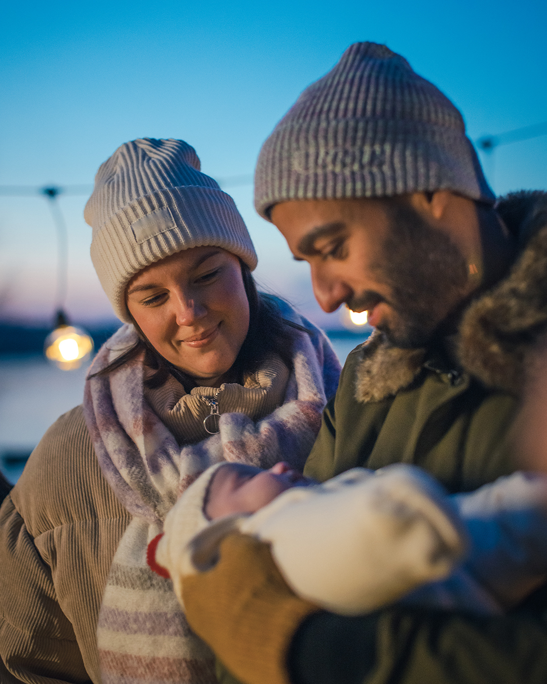 En man och en kvinna i ytterkläder står utomhus. Mannen håller i en bebis.