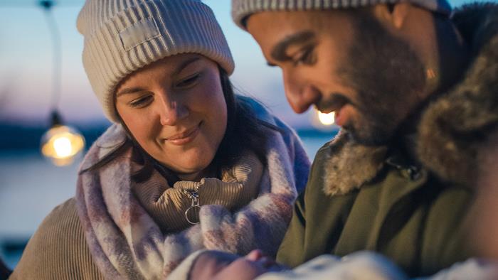 En man och en kvinna i ytterkläder står utomhus. Mannen håller i en bebis.