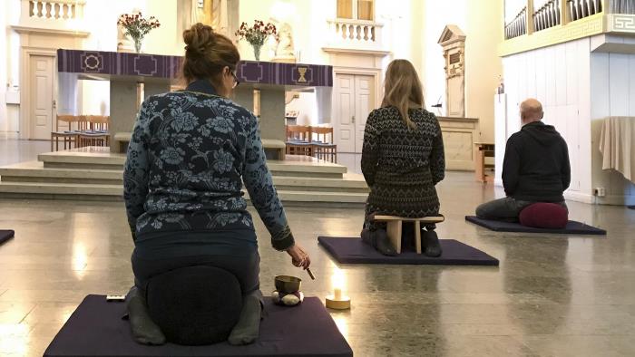 Några personer sitter på bönpallar på små mattor, på stengolvet i en kyrka.