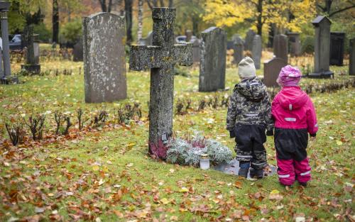 Två små barn i overaller står vid en gravplats.