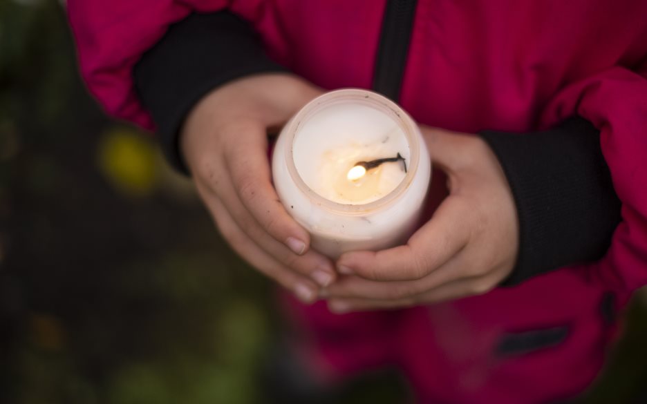 Ett litet barn håller i ett tänt gravljus.