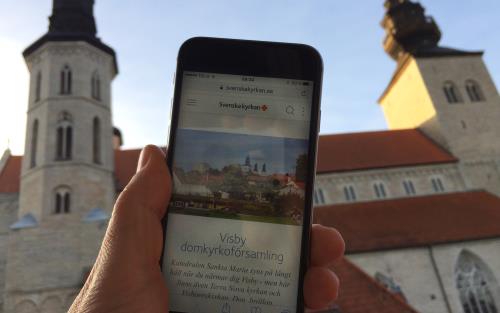 I förgrunden en mobiltelefon som surfat in på församlingens hemsida, i bakgrunden domkyrkan Sankta Maria