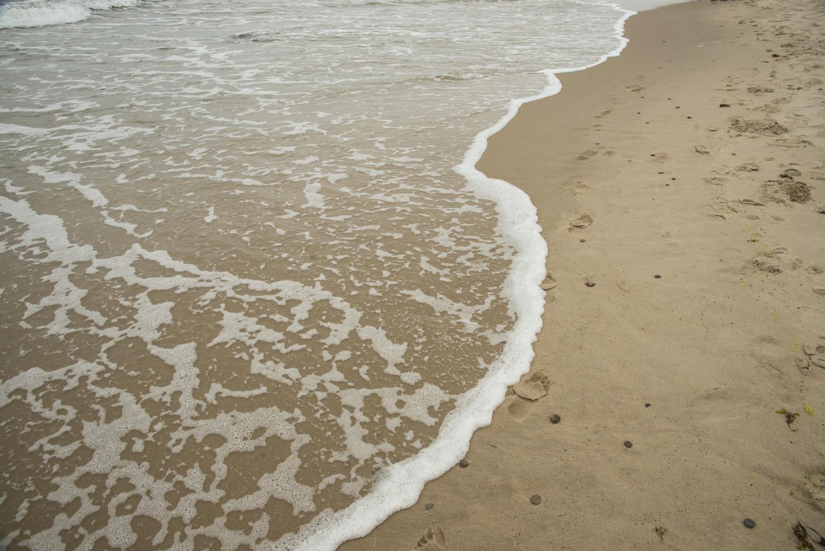 Fotspår i sanden som spolas över av en våg vid strandkanten.