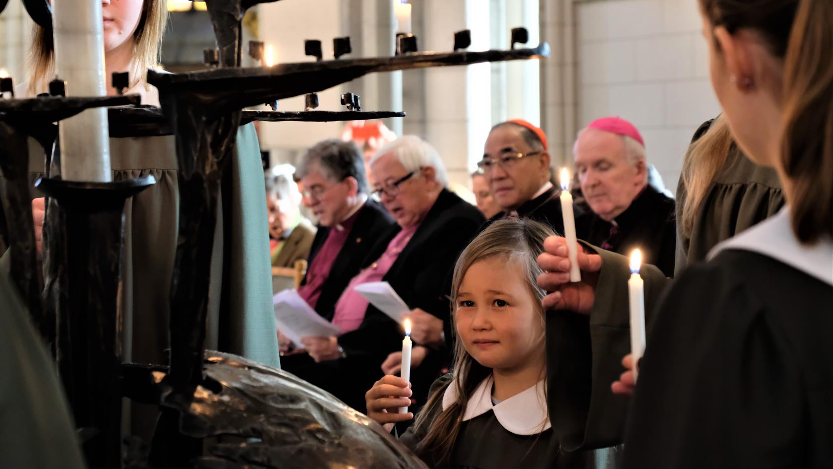 Flickor i svarta kåpor tänder ljus i Uppsala domkyrka.