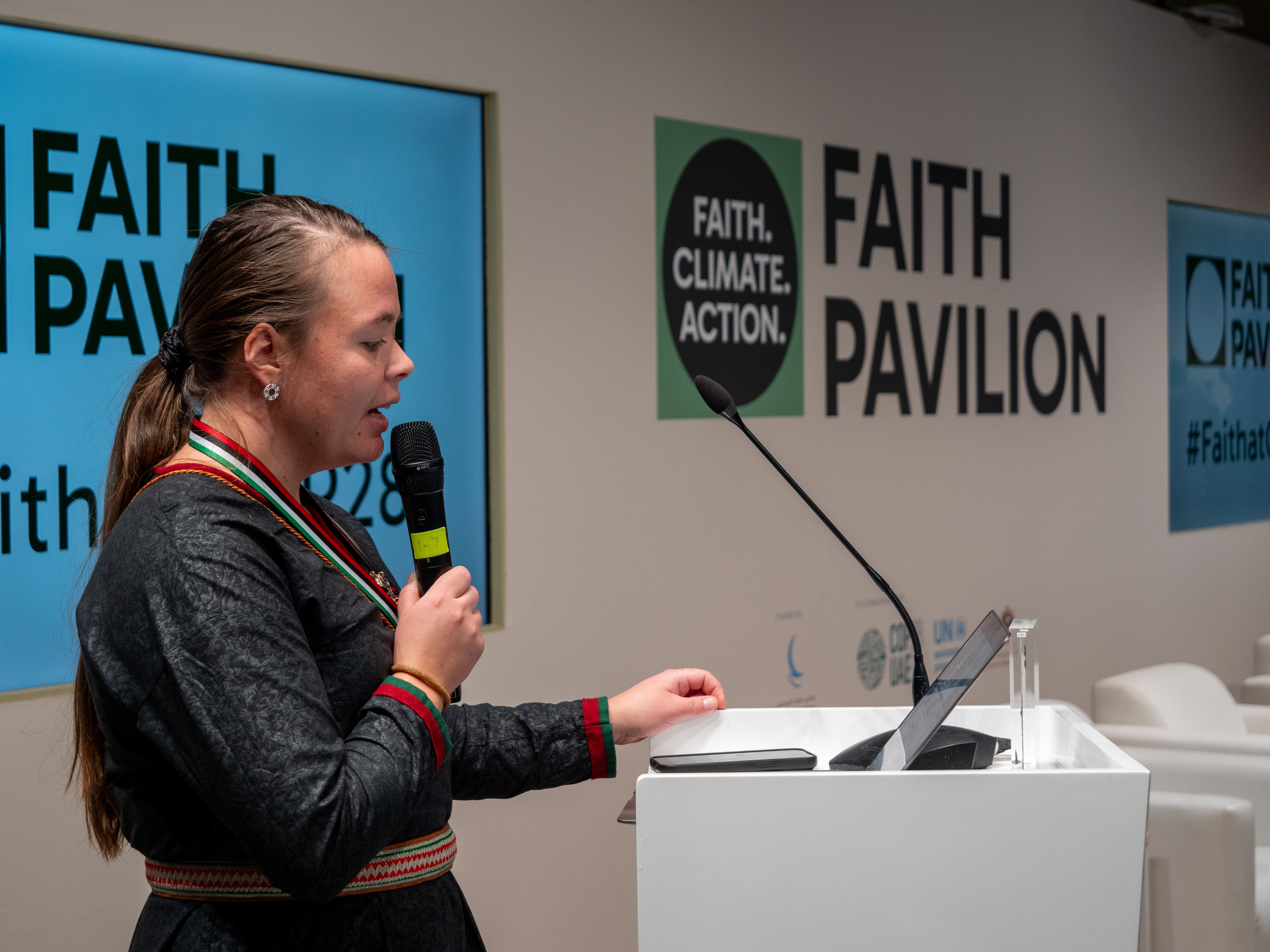Kvinna i samedräkt framför skylt med texten Faith Pavilion