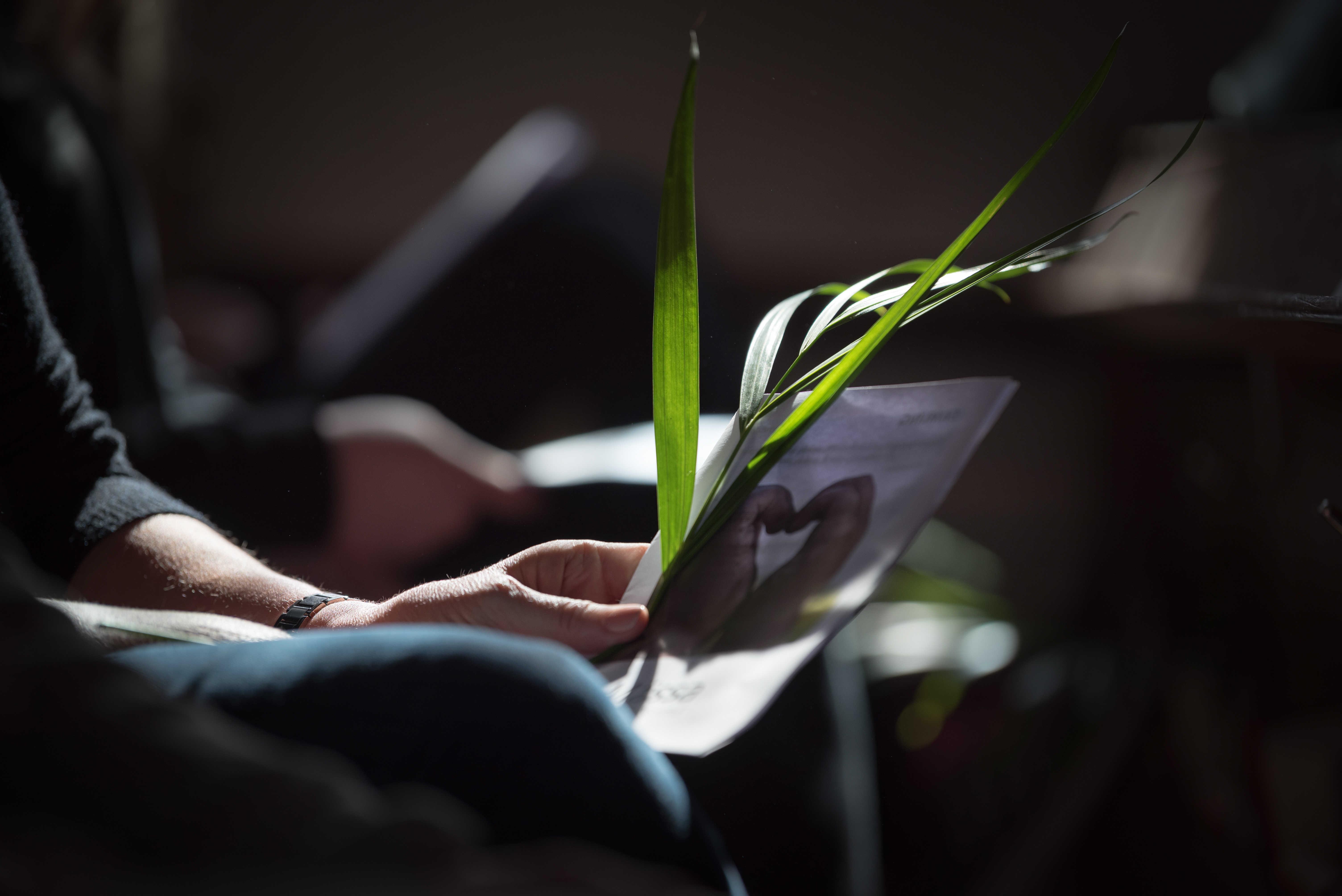 En person sitter med ett palmblad och ett häfte i händerna.