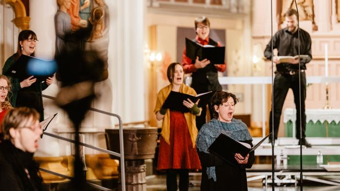 Åtta körsångare står och sjunger på coronasäkert avstånd från varandra i Umeå stads kyrka.