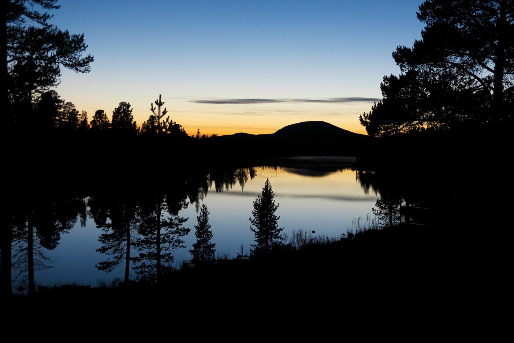 Skog och ett berg reflekteras på en stilla vattenyta i solnedgången.