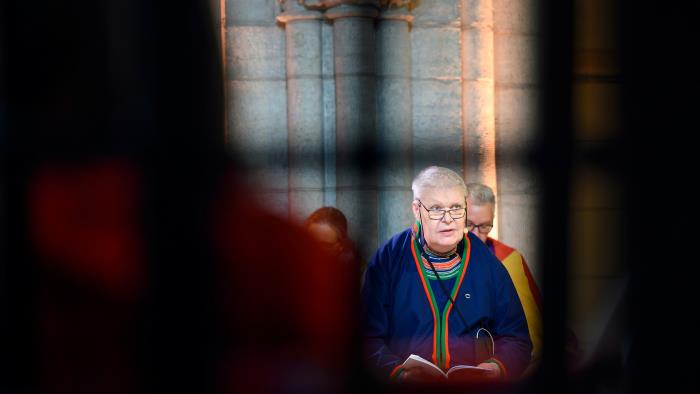 Man, klädd i samisk klädsel, framträder mellan skuggor av andra personer i en kyrka. 