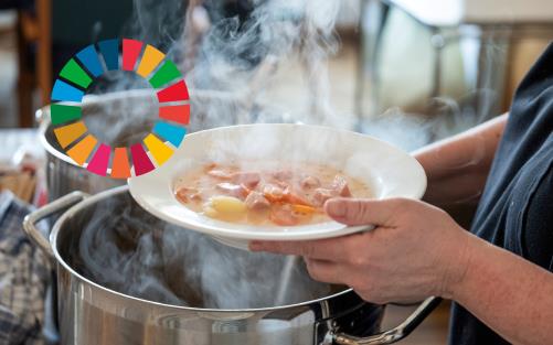 Någon tar soppa ur en stor kastrull. Till vänster i bilden syns loggan för Agenda 2030.