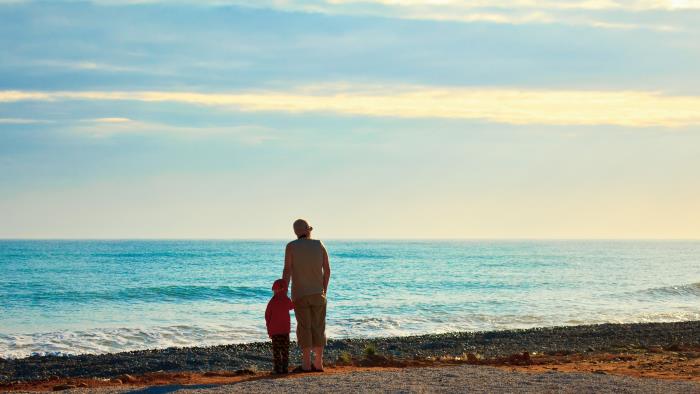 En vuxen och ett barn står vid strandkanten och tittar ut över vattnet.