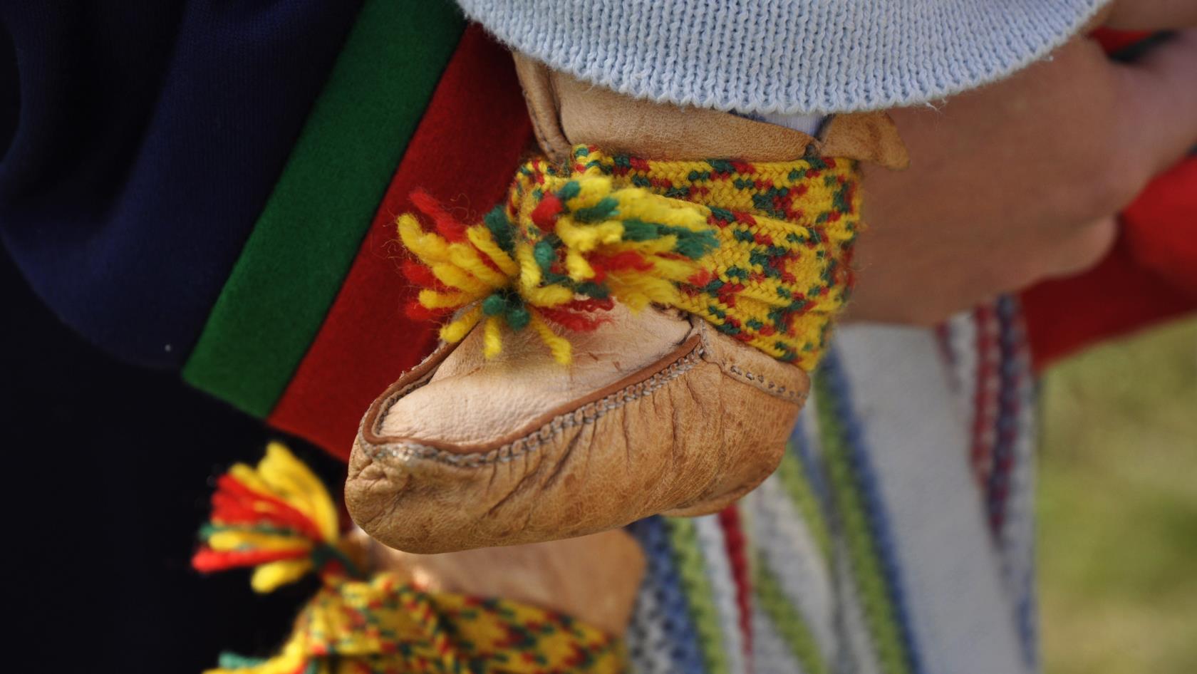 Närbild på fötterna till ett litet barn som blir buret och som har samiska skor.