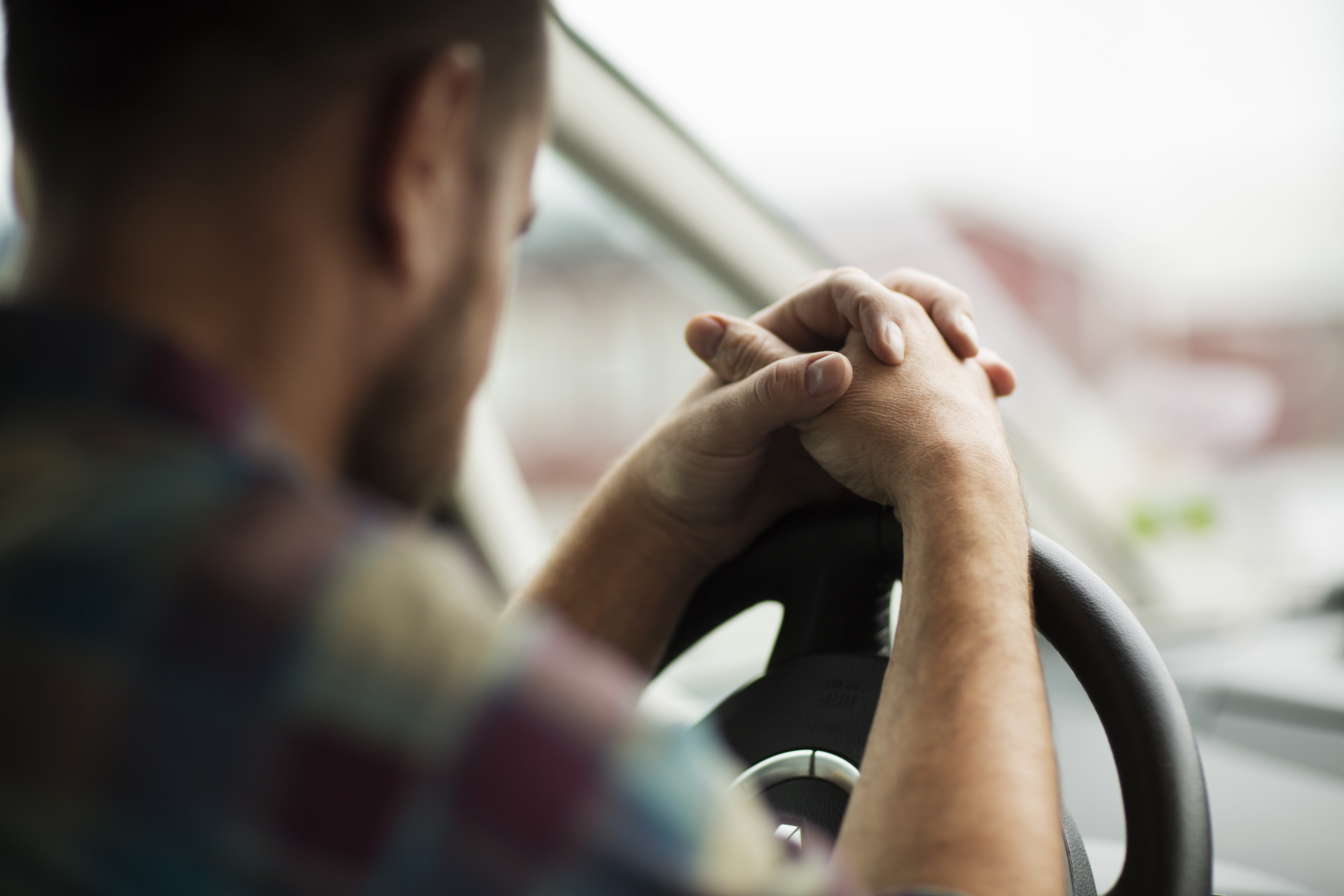 En man sitter i bilen med händerna knäppta på ratten.