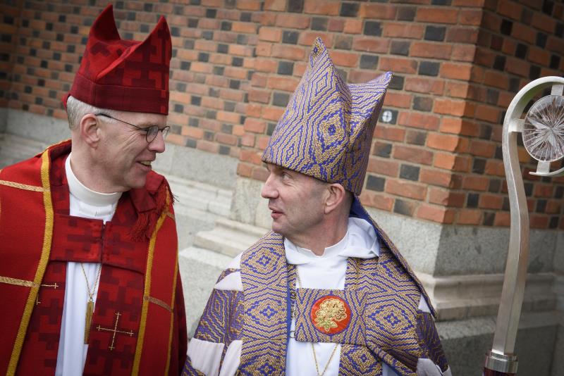 Biskoparna Martin och Fredrik Modéus står i ämbetsdräkter utanför Uppsala domkyrka.