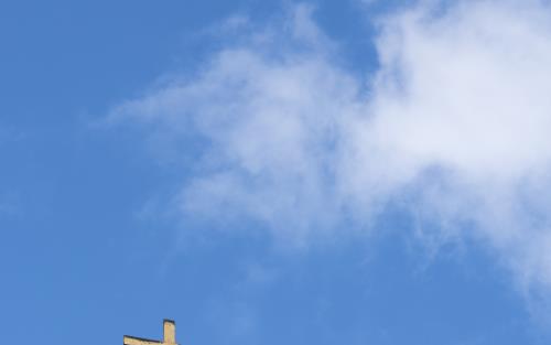 Ett kors på ett kyrktak mot blå himmel.