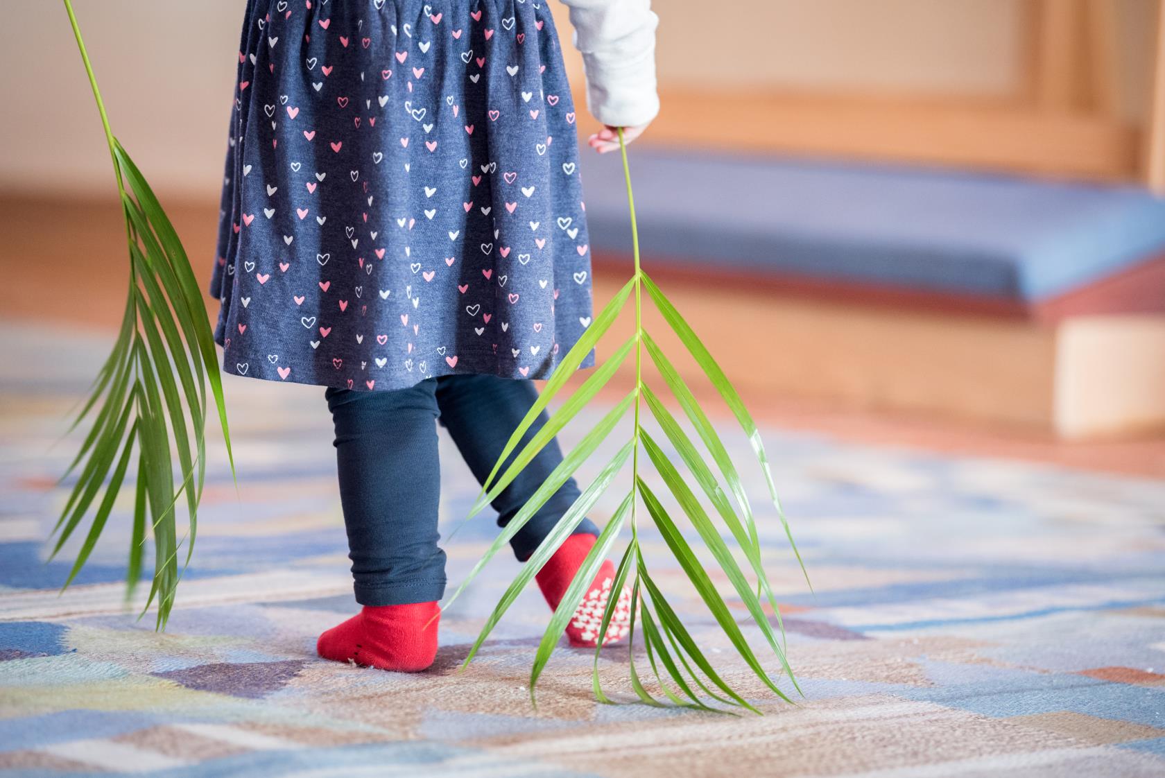 Ett barn i strumplästen går med palmblad i händerna.