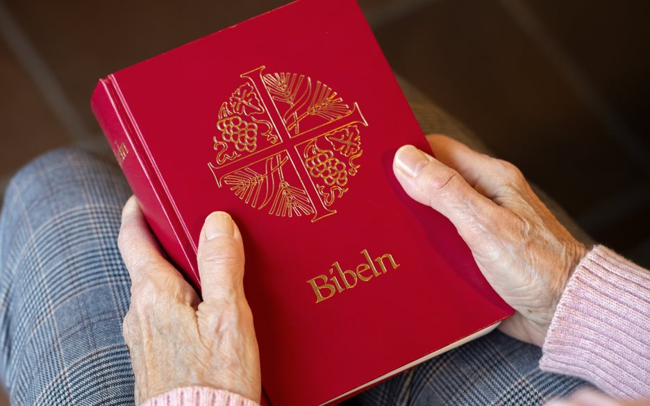 En person sitter i en kyrkbänk med en bibel i knät.