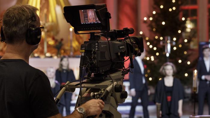 En kamera man står bakom en TV-kamera och spelar in en julkonsert.