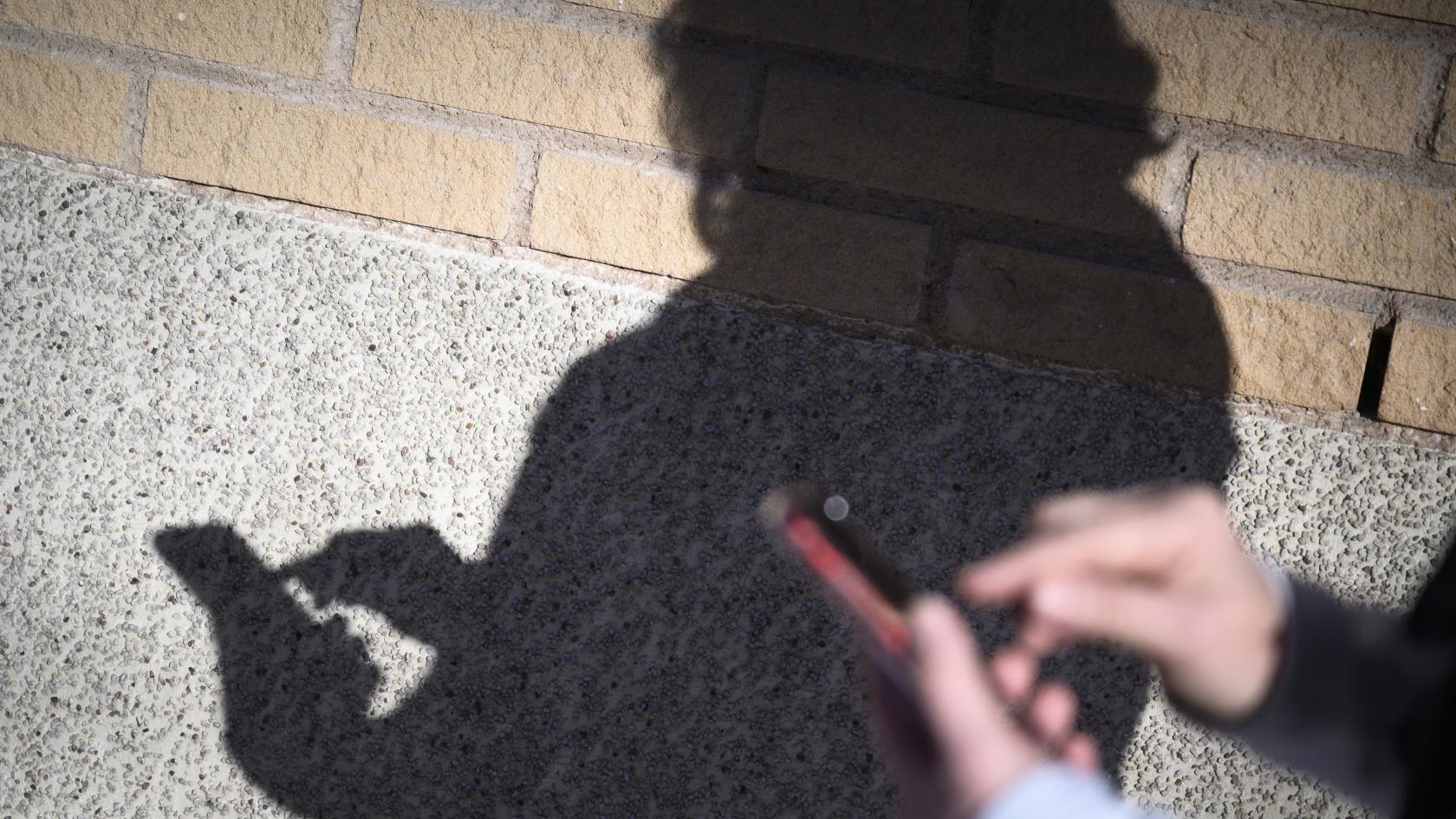 En skugga på en tegelvägg av någon som skriver på sin mobiltelefon.