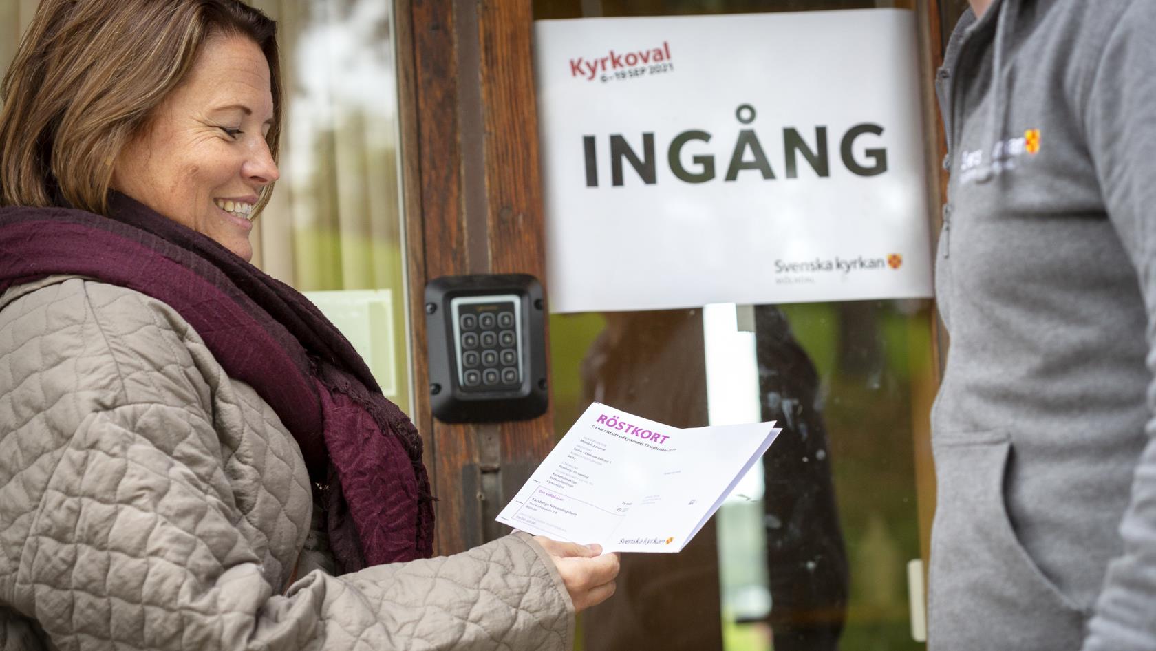 En kvinna visar upp sitt röstkort utanför ingången till en vallokal för Kyrkovalet.