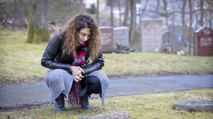 En kvinna på en kyrkogård sitter på huk vid en minnessten.